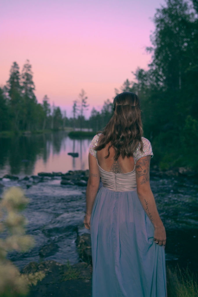 Jente i kjole ved vannet og solnedgang.